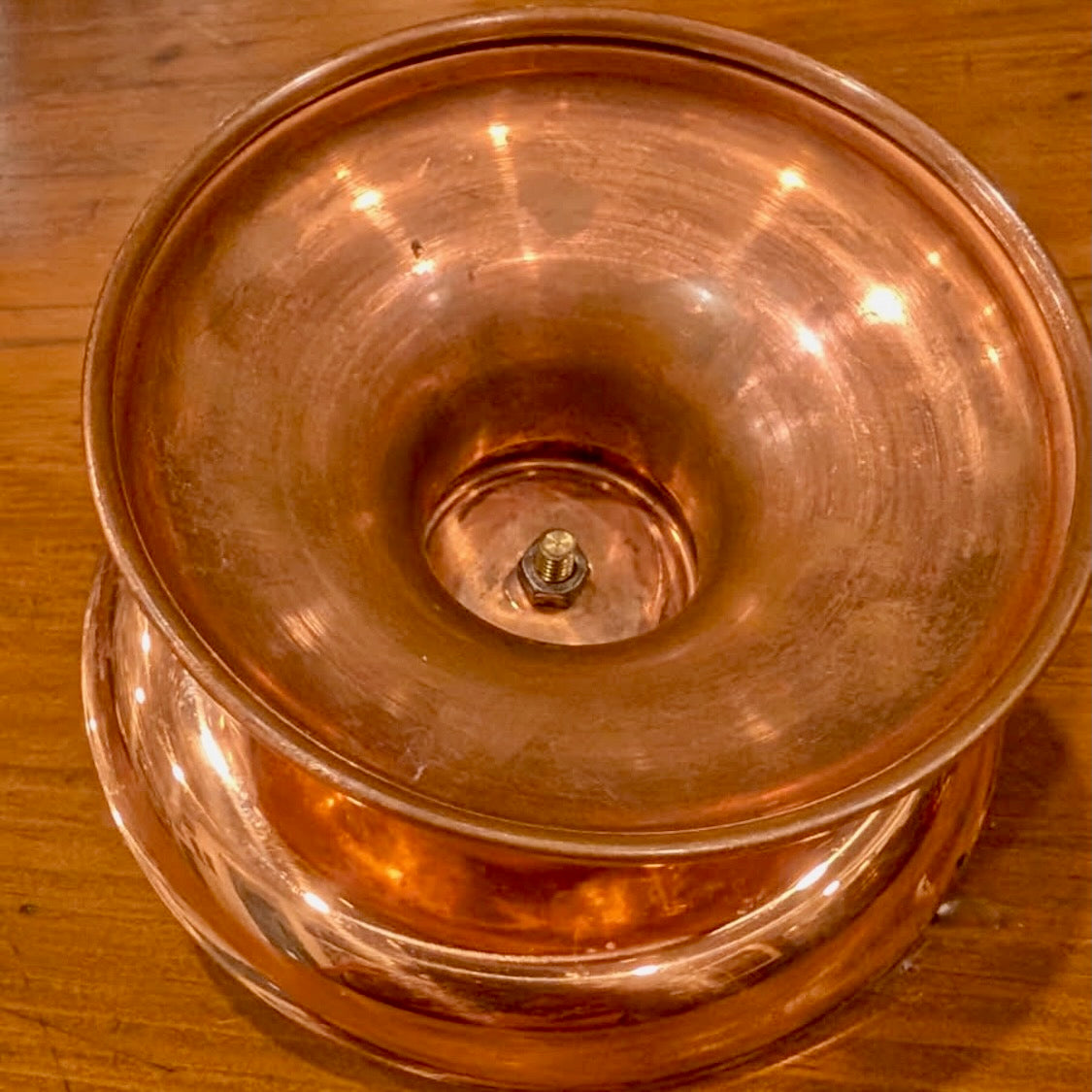 The base of a copper candleholder showing the bold joint the top with the pedestal base on a wooden surface