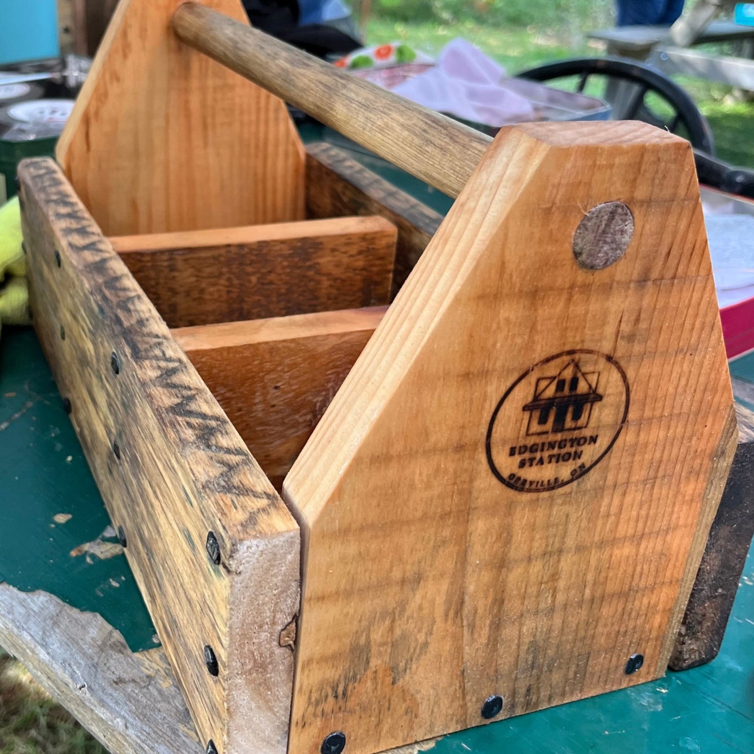 A hand-made wooden tote box with with a branded Edgington Station logo on a green table