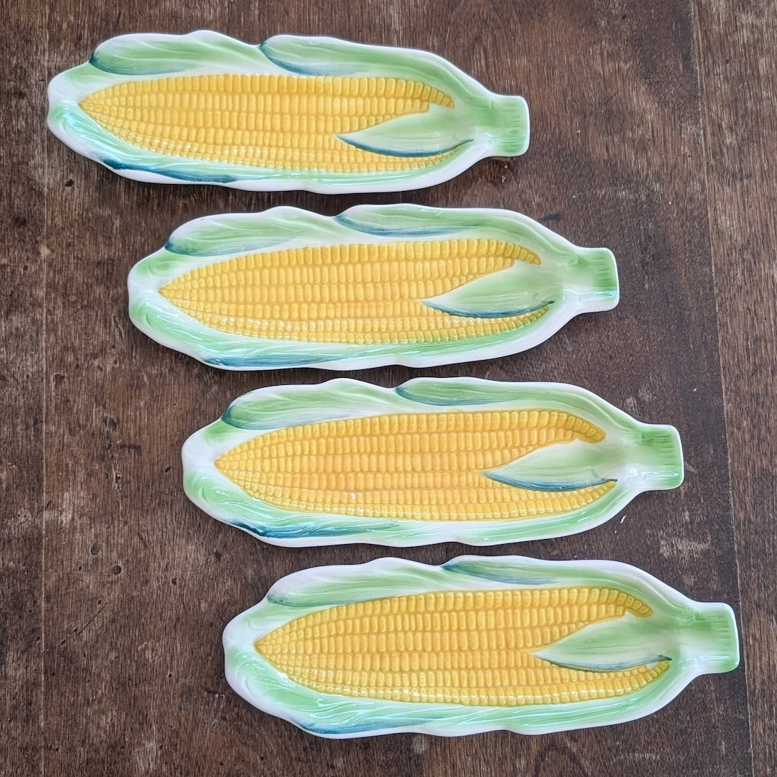 4 green and yellow ceramic dishes shaped like cobs of corn on a wooden surface