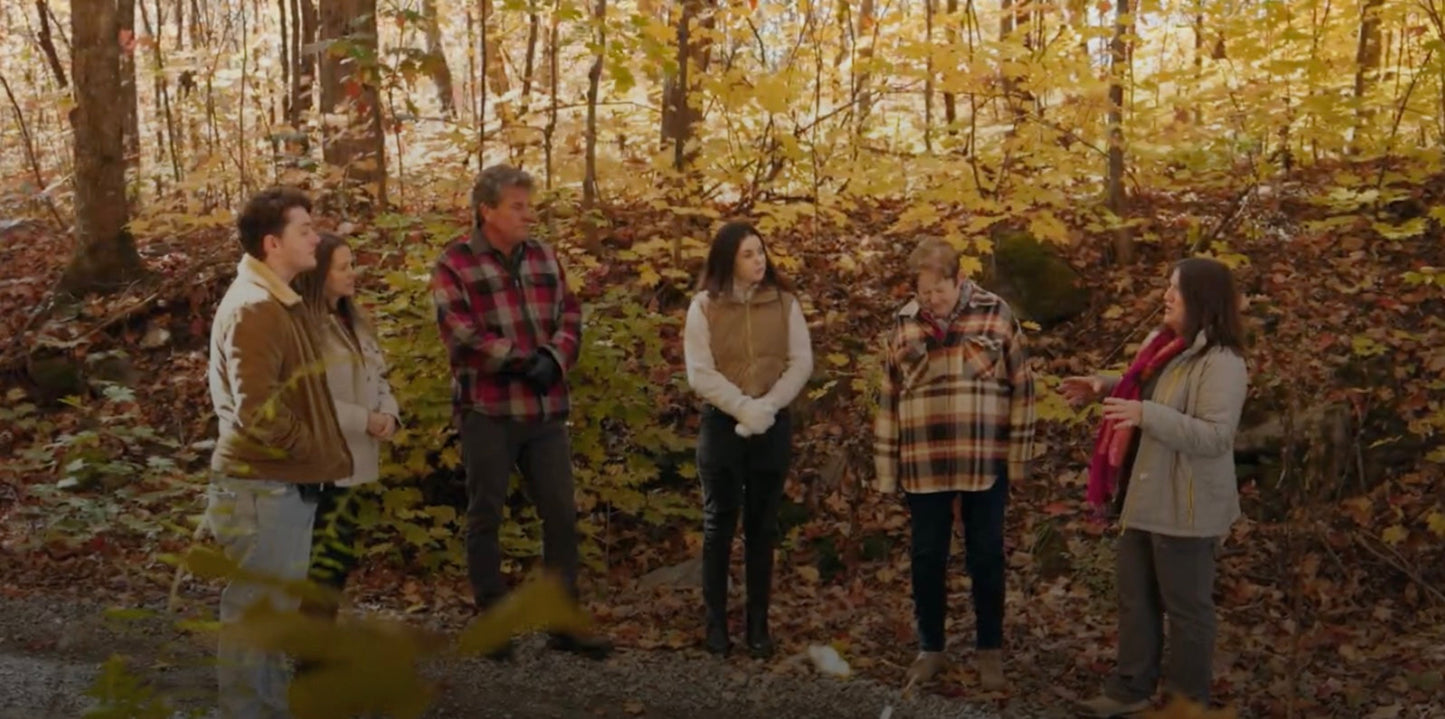 A small group of people standing in a forest listening to a guide, surrounded by autumn leaves