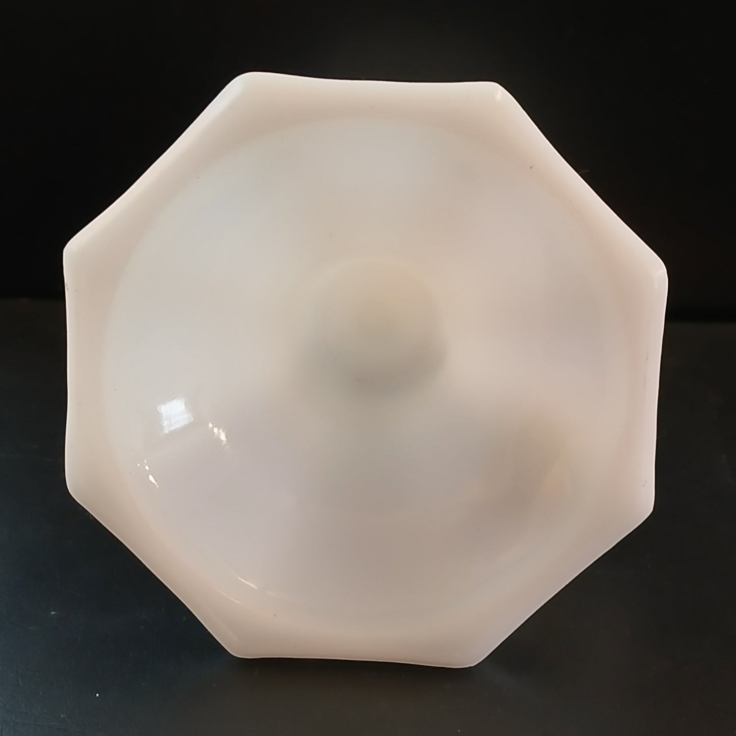 Octagonal white glass base of the candle holder with no markings present on a black background