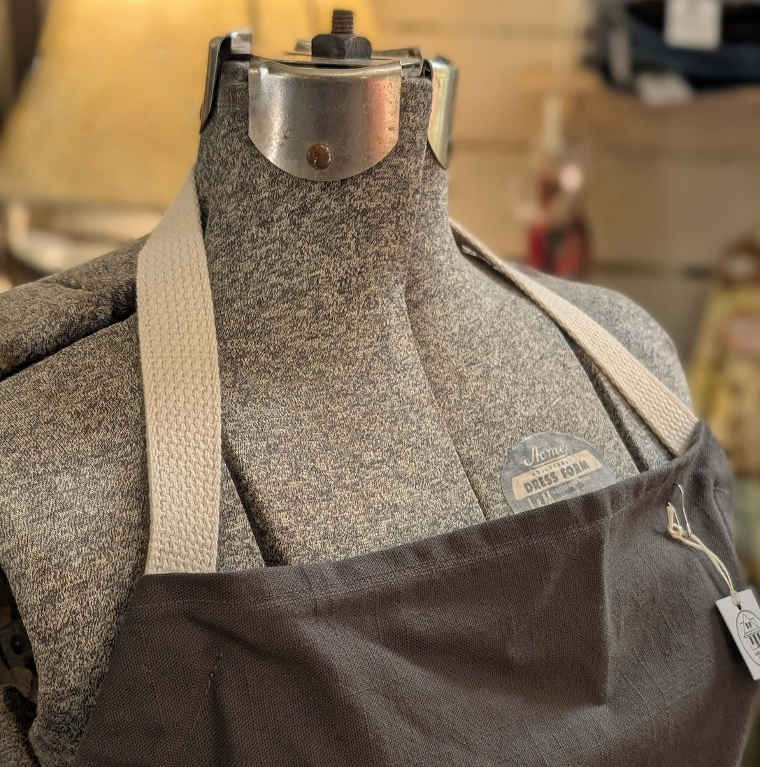 Detail of strap of neckline of a grey linen apron on a mannequin with a blurred background