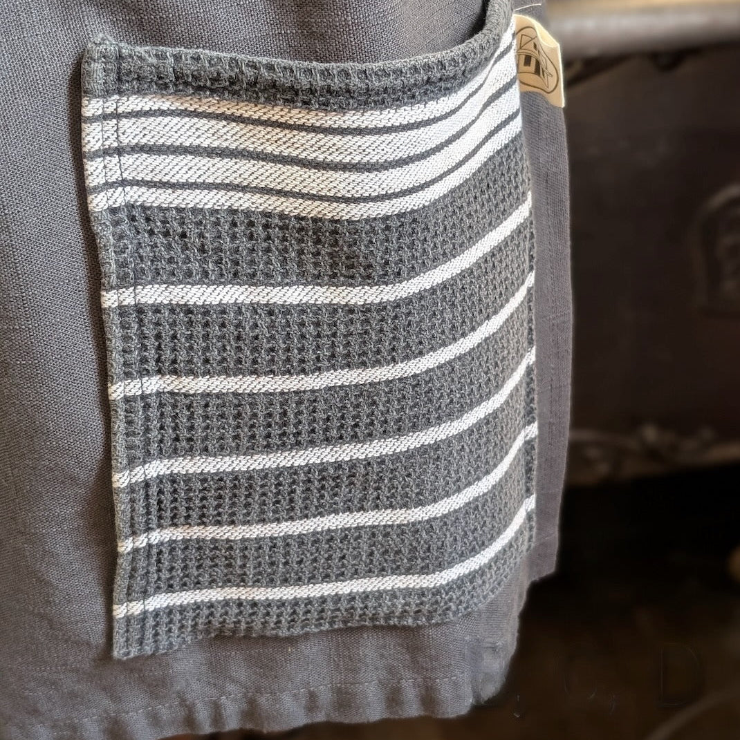 Detail of a grey and white striped pocket on a grey linen apron against a blurred background
