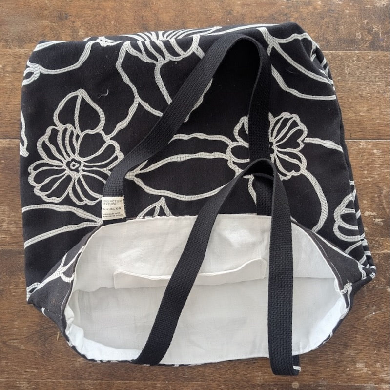A black fabric tote bag with a vivid white geometric pattern  and a white interior shown on a wooden background