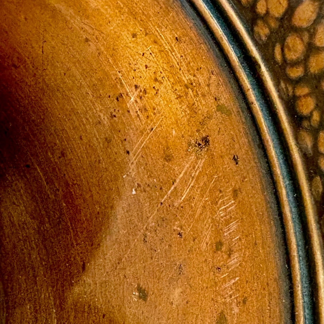 Close up view of minor scratches and small dark spots on a copper bowl