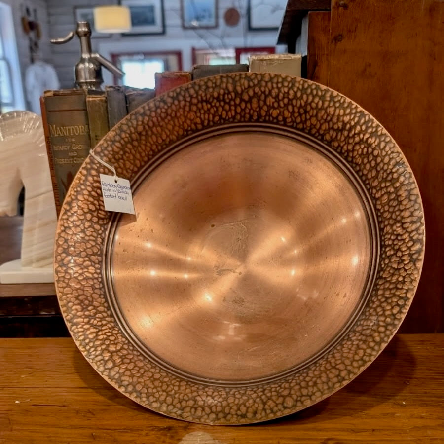 A copper pedestal bowl with a hammered textured rim on a wooden surface