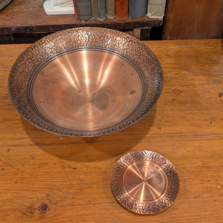 Top view of a copper pedestal bowl and pillar candleholder on a wooden on a wooden surface with books in the background