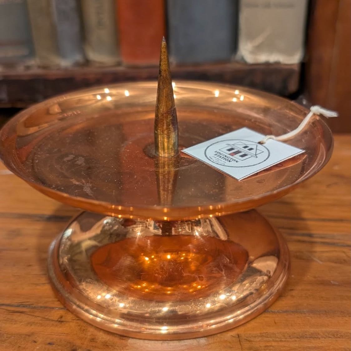 The top of a copper candleholder with a shop tag showing some scratches  and dark marks on the finish