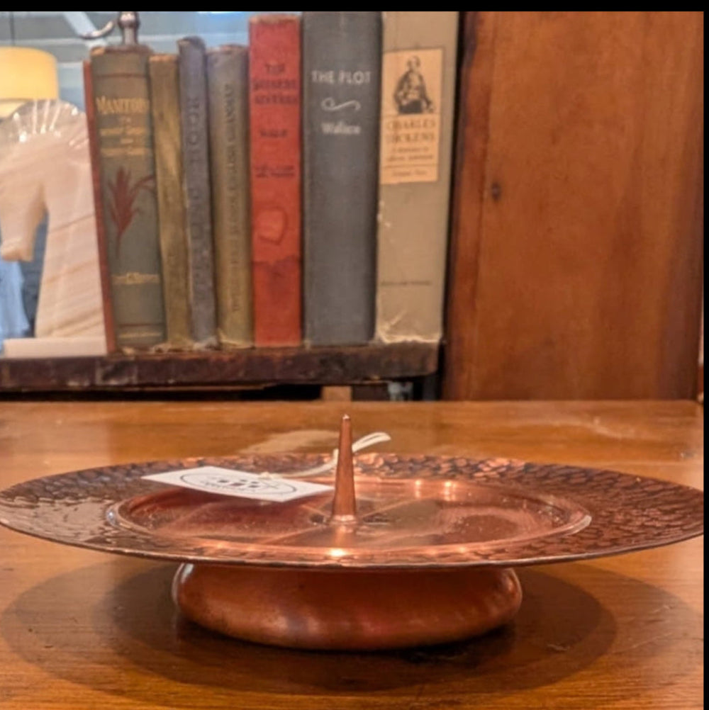 Side view of a footed copper pillar candleholder on a wooden surface with old books in the background