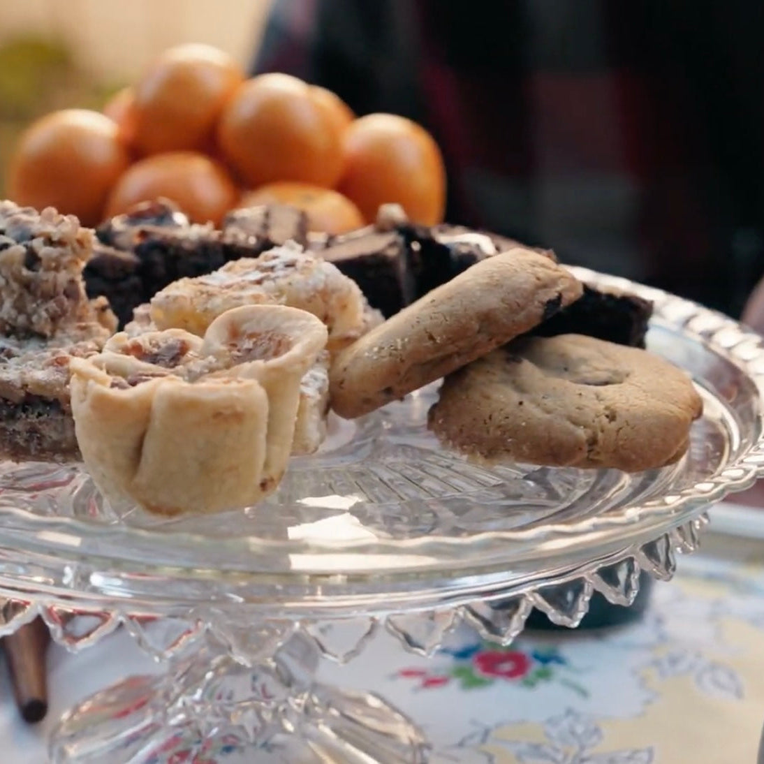 An appetizing assortment of tarts and pastries on an antique cake stand next to a bowl of clementines 
