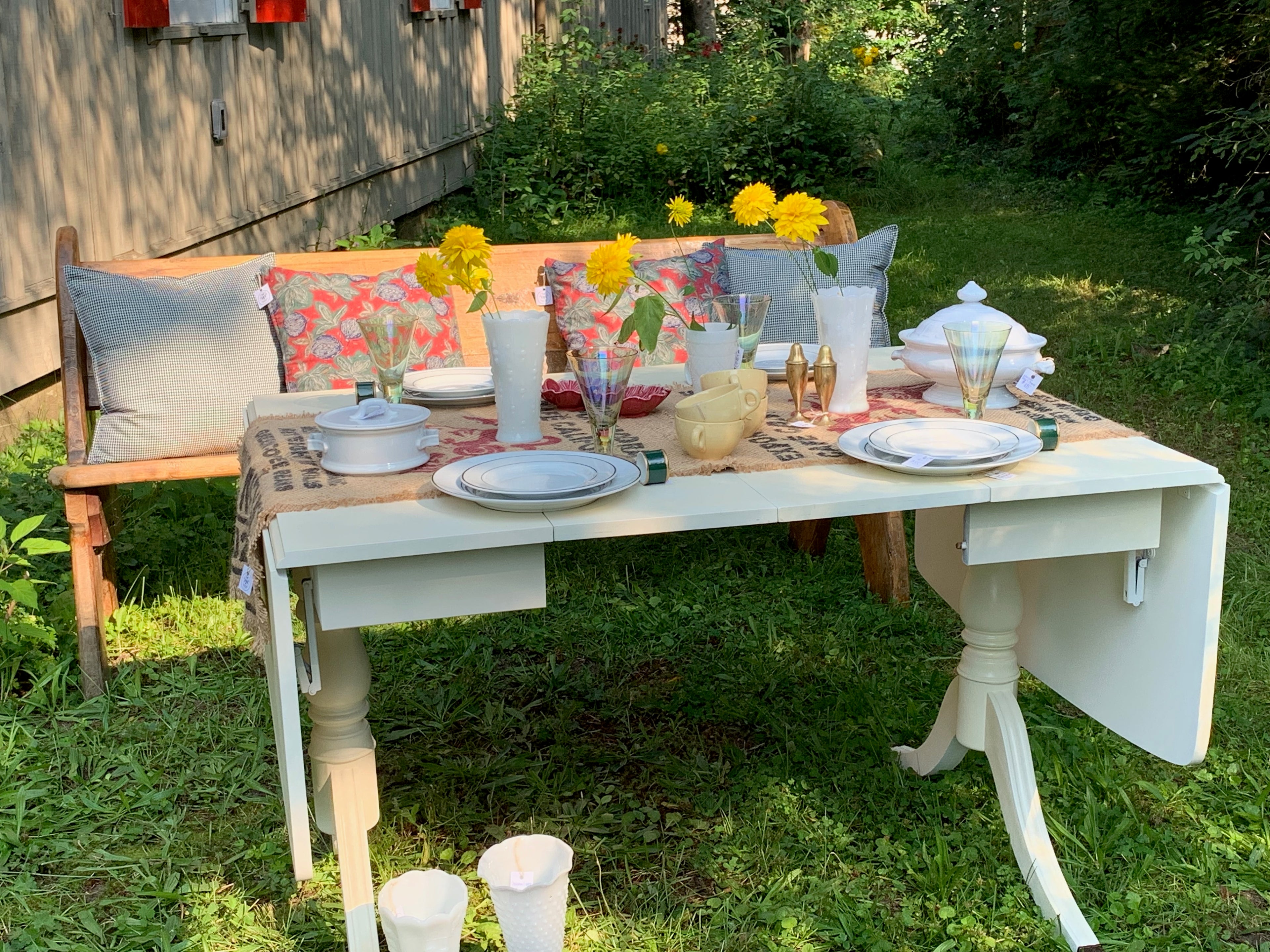 A refinished vintage table  in the gardenset with antique dishes next to a bench with  hand-made cushions 