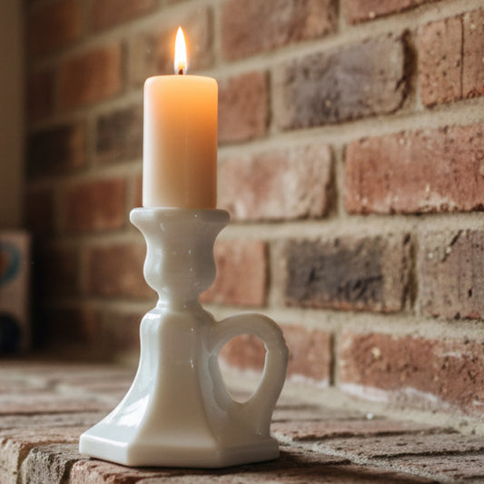 White milk glass candle holder with a lit candle on a brick mantle
