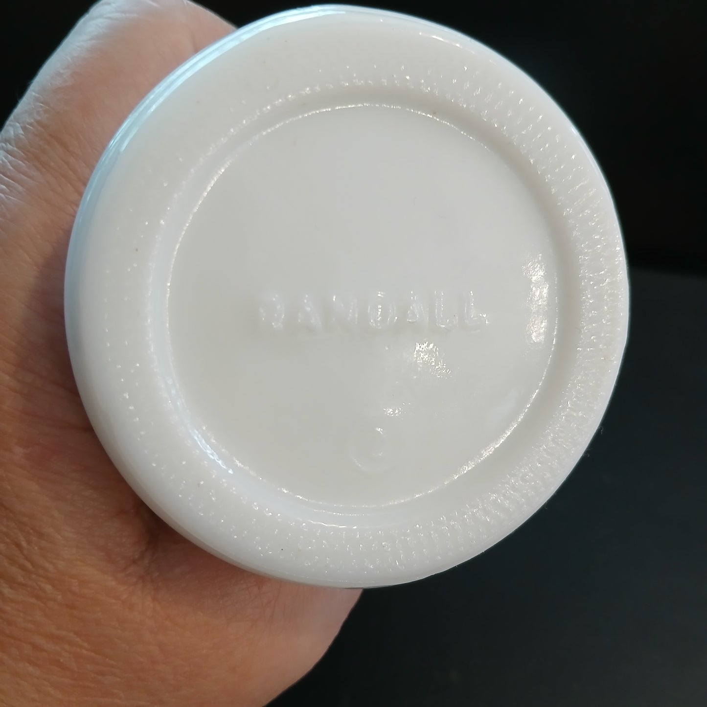 Small white glass vase marked Randall held in a hand against a dark background