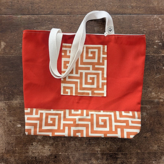Hand-sewn orange tote bag  with bronze geometric pattern and a white strap on a wooden surface