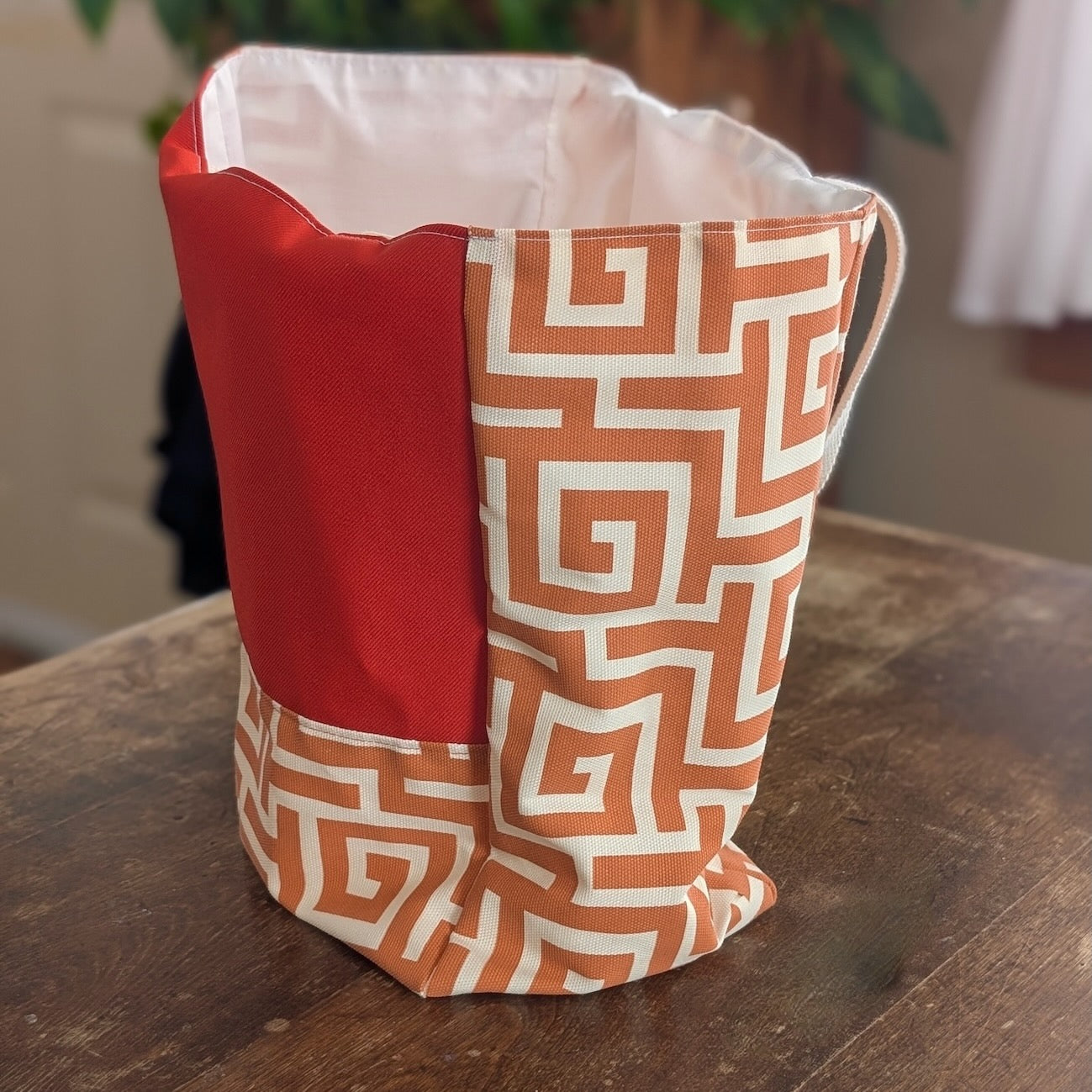 A small tote bag made with salvaged vintage fabric printed with an orange and white geometric pattern sitting upright and open on a wooden surface