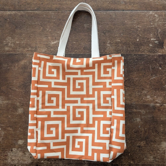A small tote bag made with salvaged vintage fabric printed with an orange and white geometric pattern shown on a wooden surface