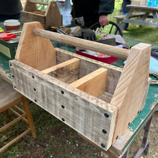 A homemade wooden tool carrier on a table outdoors with people doing woodworking in the background