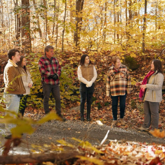 Group of people standing on a path in a forest with autumn foliage.