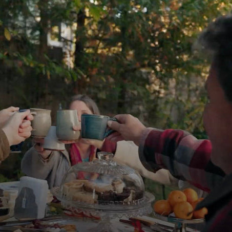 a group raising mugs at a table outdoors with trees in the background