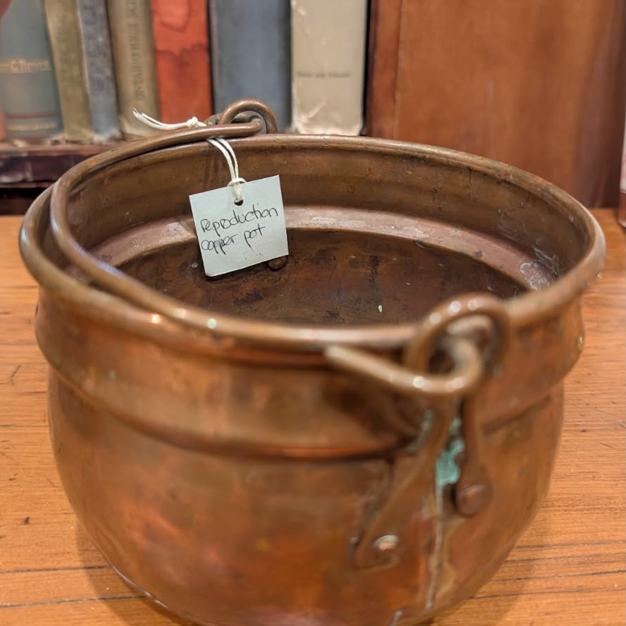 Vintage copper and brass pot showing handle connections on a wooden surface