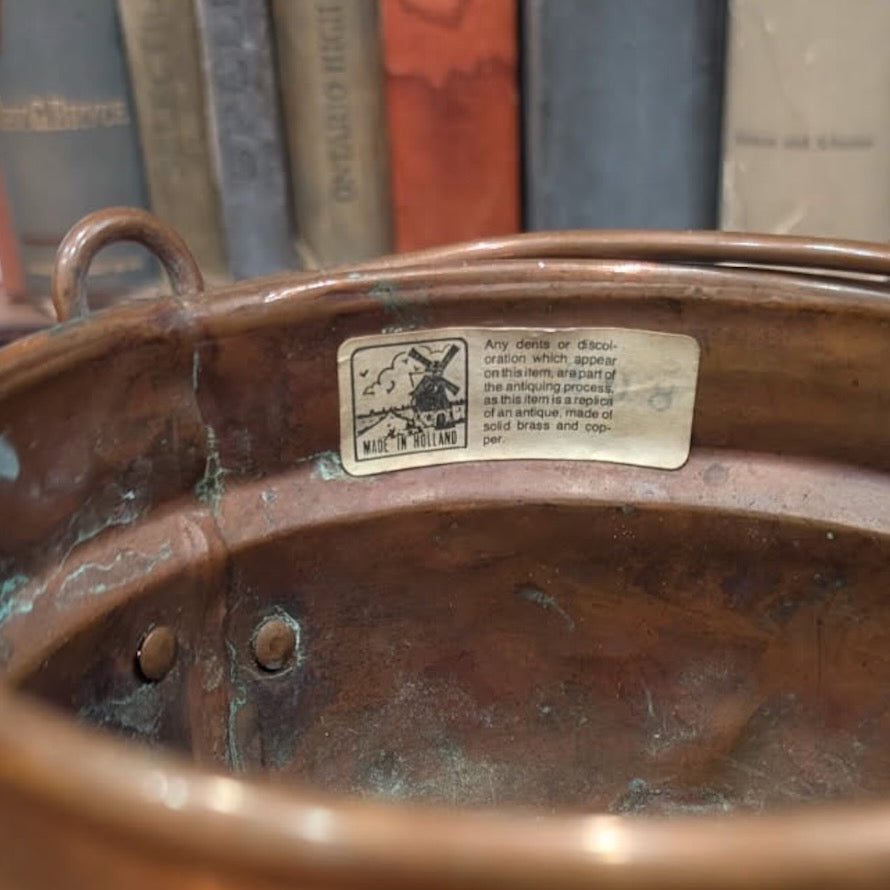 Close-up of the label on a copper and brass pot with books in the background