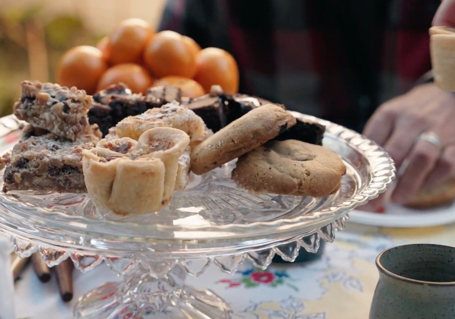 An appetizing assortment of tarts and pastries on an antique cake stand next to a bowl of clementines 