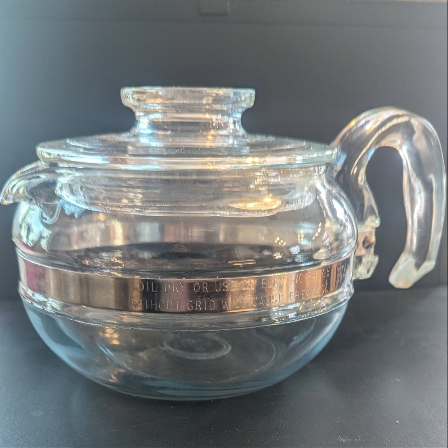 A glass Pyrex Teapot on a shiny black table