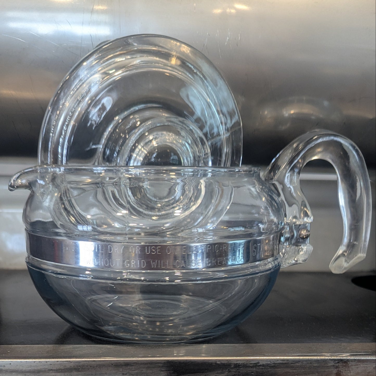 A clear glass teapot with the lid askew sitting on a shiny surface