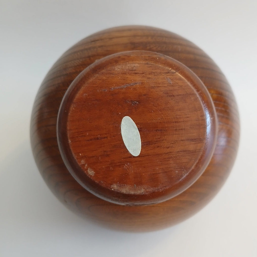 Base of teak orb dish showing illegible original sticker on a white background