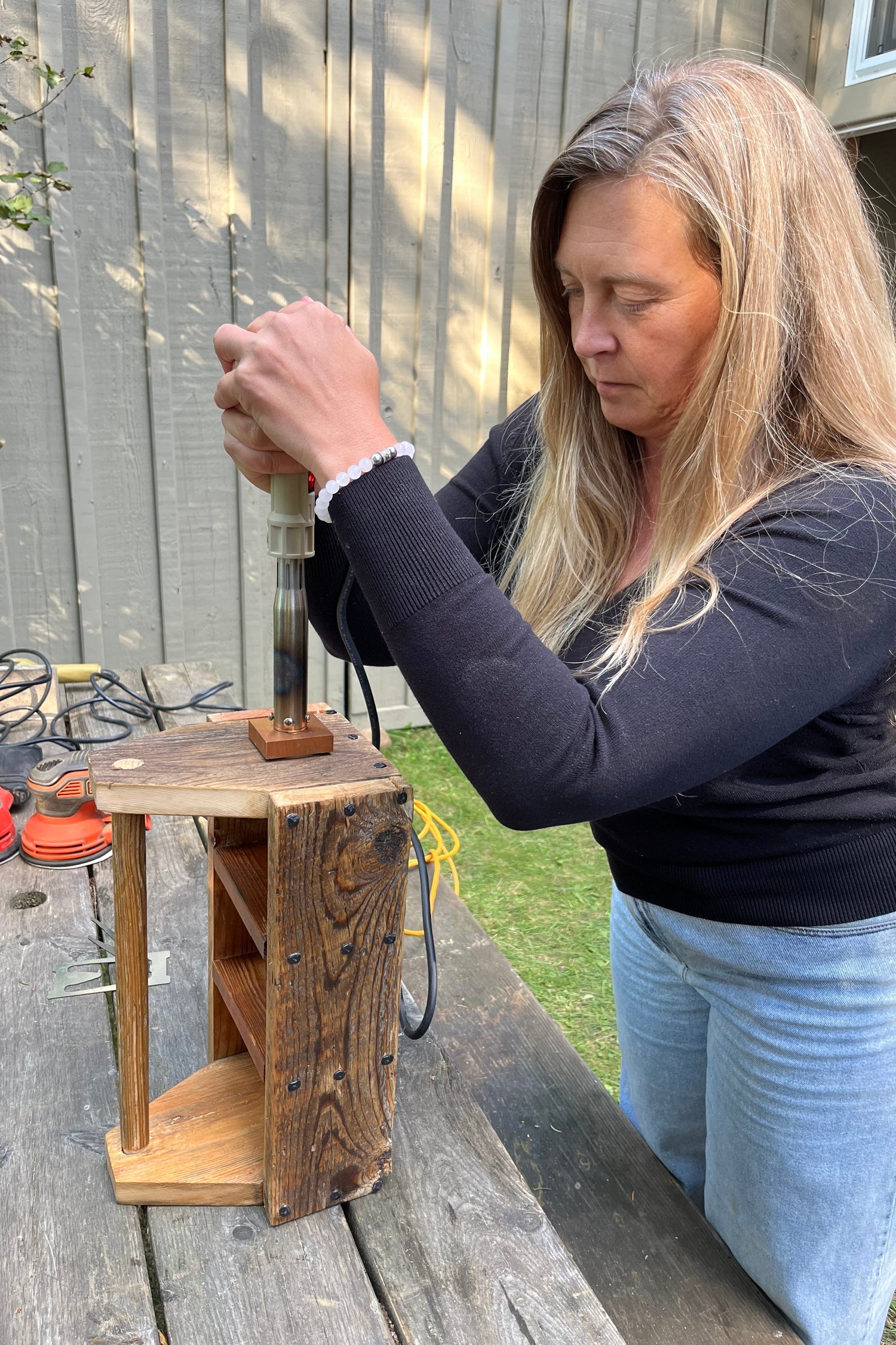 A woman at an outside table brands a logo onto the  wooden toolbox she has created